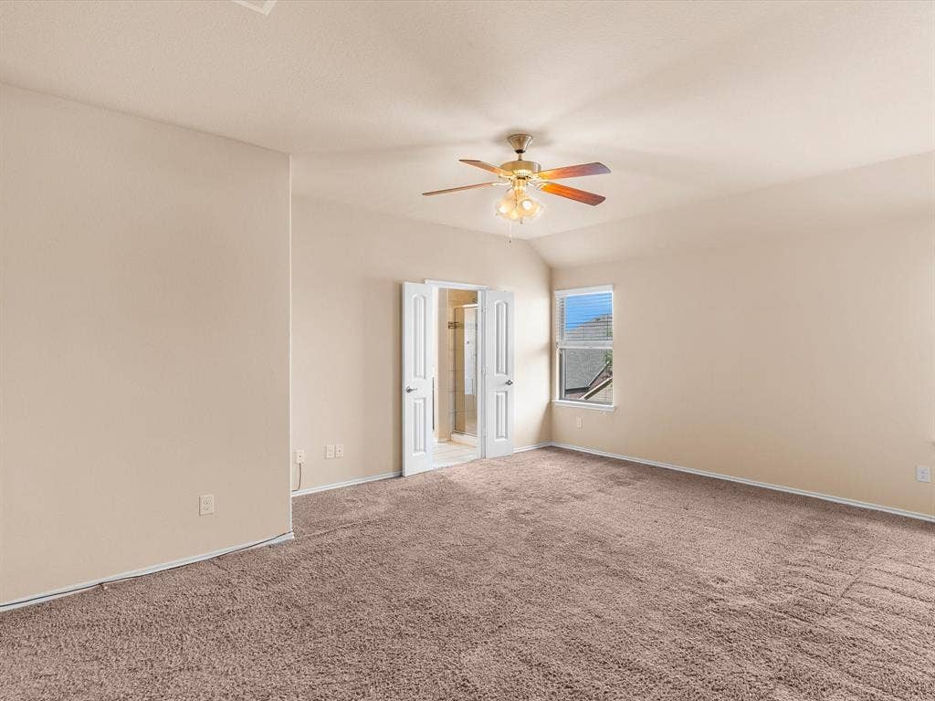 Spacious interior featuring neutral-toned carpeting, vaulted ceilings, and a center-mounted ceiling fan with light fixture