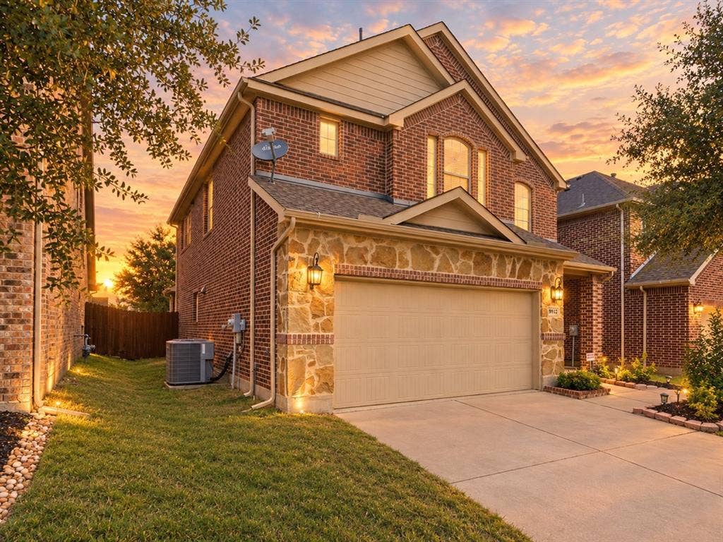 Multi-level exterior featuring red brick masonry, natural stone accents, a multi-gabled roofline, and an attached two-car garage