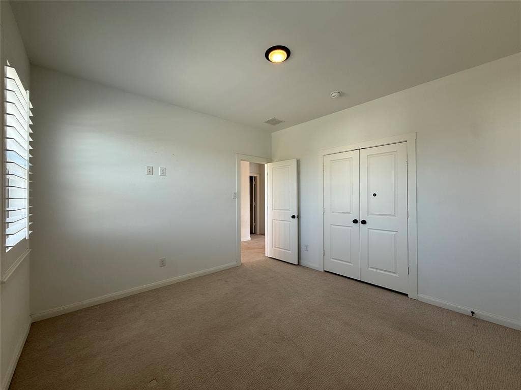 12905 Yale Court, Frisco, TX 75035 Interior room featuring neutral wall-to-wall carpeting, white walls, plantation shutters, dual-panel closet doors with matte black hardware, and an overhead flush-mount light fixture