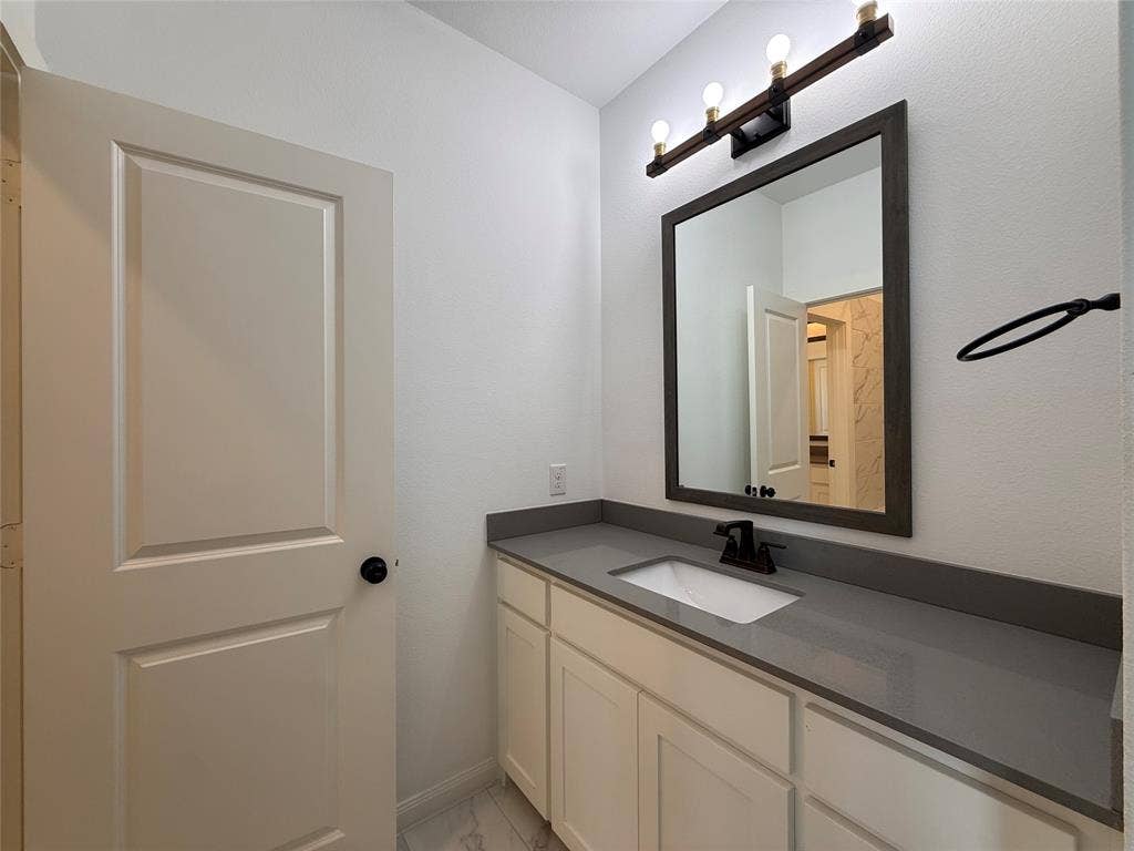 12905 Yale Court, Frisco, TX 75035 Bathroom vanity featuring shaker-style cabinetry, quartz countertop, undermount sink, dark-finish faucet, and a wall-mounted light fixture
