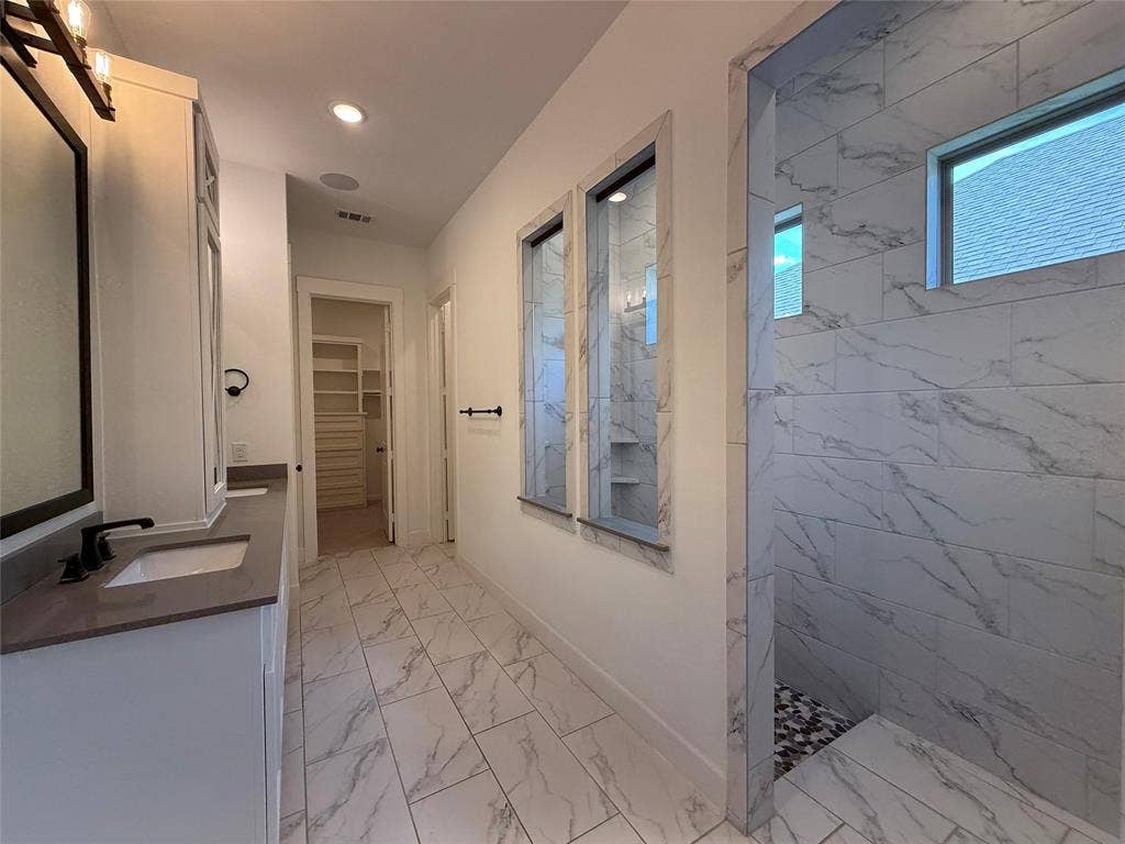 12905 Yale Court, Frisco, TX 75035 Dual vanity featuring solid-surface countertops, walk-in shower with stone-patterned tile, porcelain tile flooring, and integrated glass partitioning