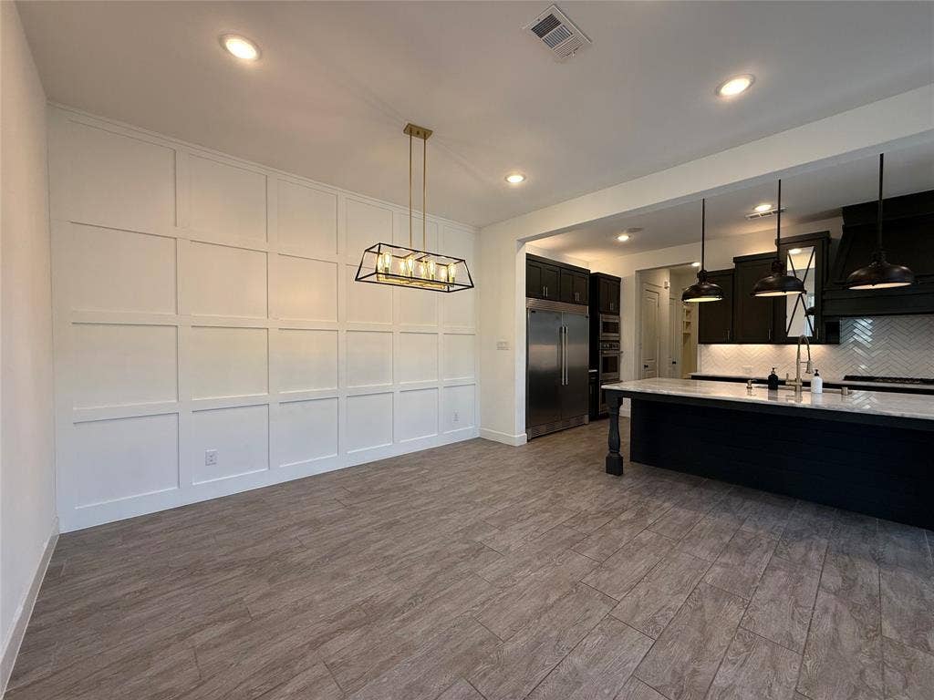 12905 Yale Court, Frisco, TX 75035 Grid-pattern wainscoting, wood-finish flooring, recessed lighting, rectangular chandelier, and a kitchen island with a stone countertop