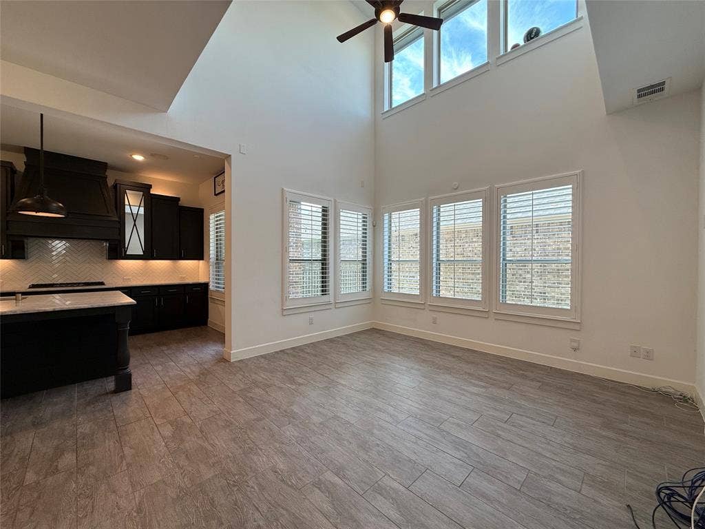 12905 Yale Court, Frisco, TX 75035 Double-height vaulted ceilings featuring clerestory windows, wood-finish tile flooring, plantation shutters, and a kitchen equipped with dark cabinetry, a center island, and a herringbone-patterned backsplash