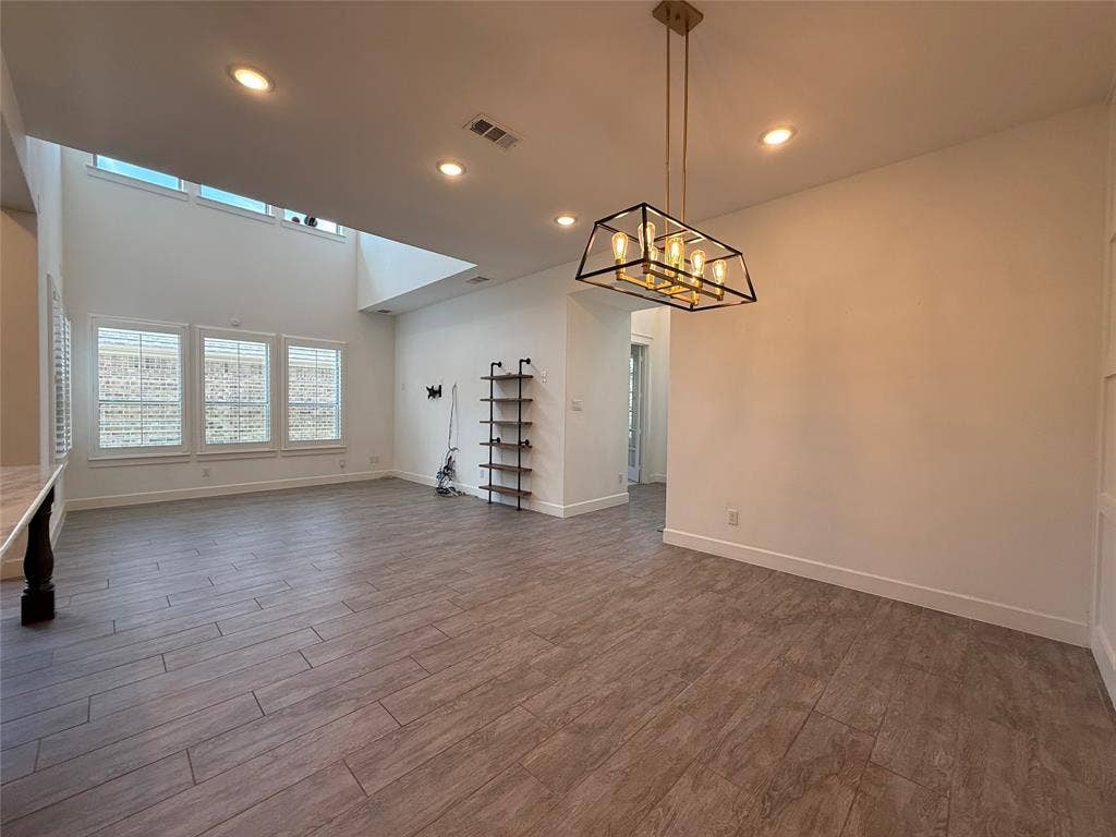 12905 Yale Court, Frisco, TX 75035 Open-concept space featuring double-height ceilings, wood-finish tile flooring, recessed lighting, and a geometric-frame pendant light fixture