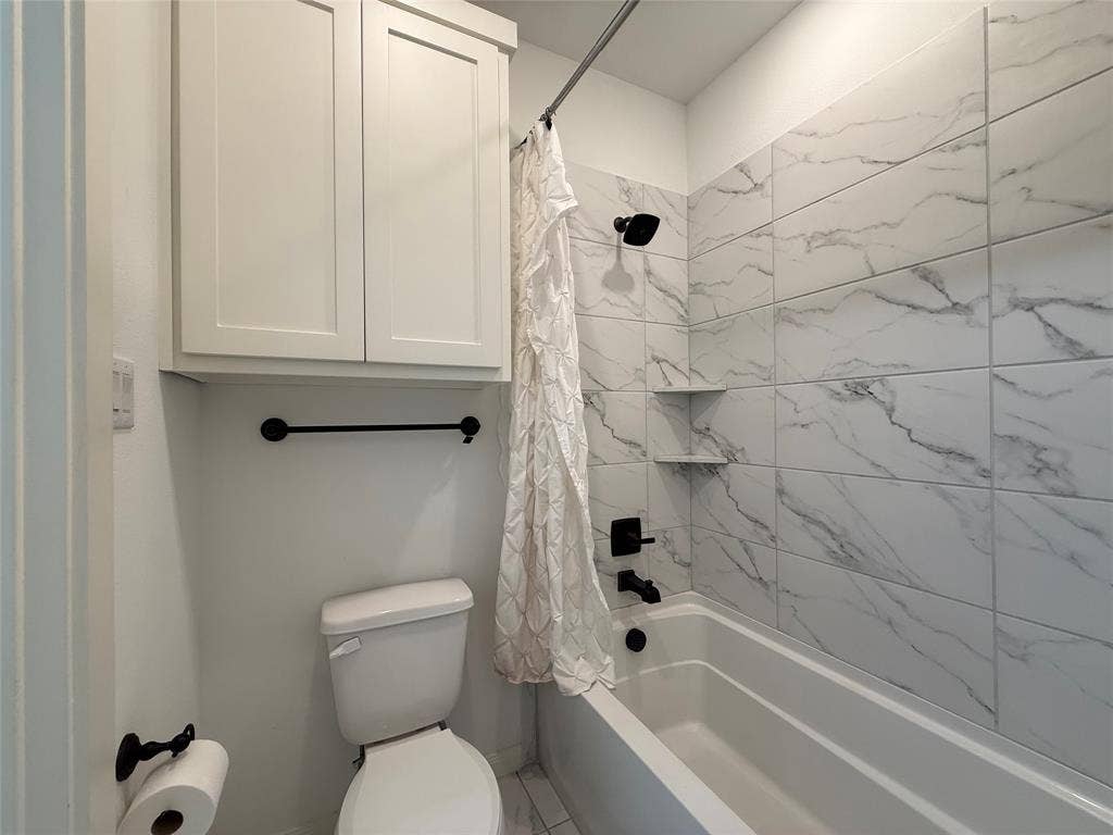 12905 Yale Court, Frisco, TX 75035 Full bathroom featuring white shaker-style wall cabinetry, large-format tile surround with integrated shelving, and matte black plumbing fixtures