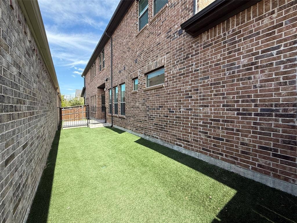 12905 Yale Court, Frisco, TX 75035 Exterior side yard featuring brick masonry construction, synthetic turf, and a metal security gate