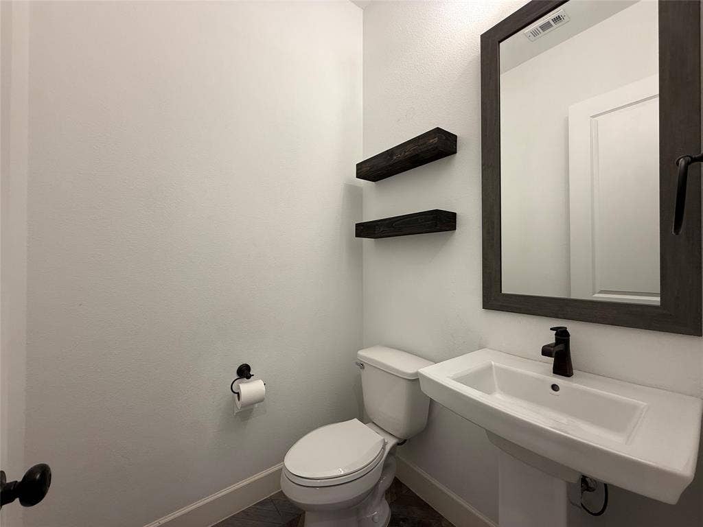 12905 Yale Court, Frisco, TX 75035 Pedestal sink with matte black faucet, wall-mounted dark wood-finish shelving, and a framed vanity mirror