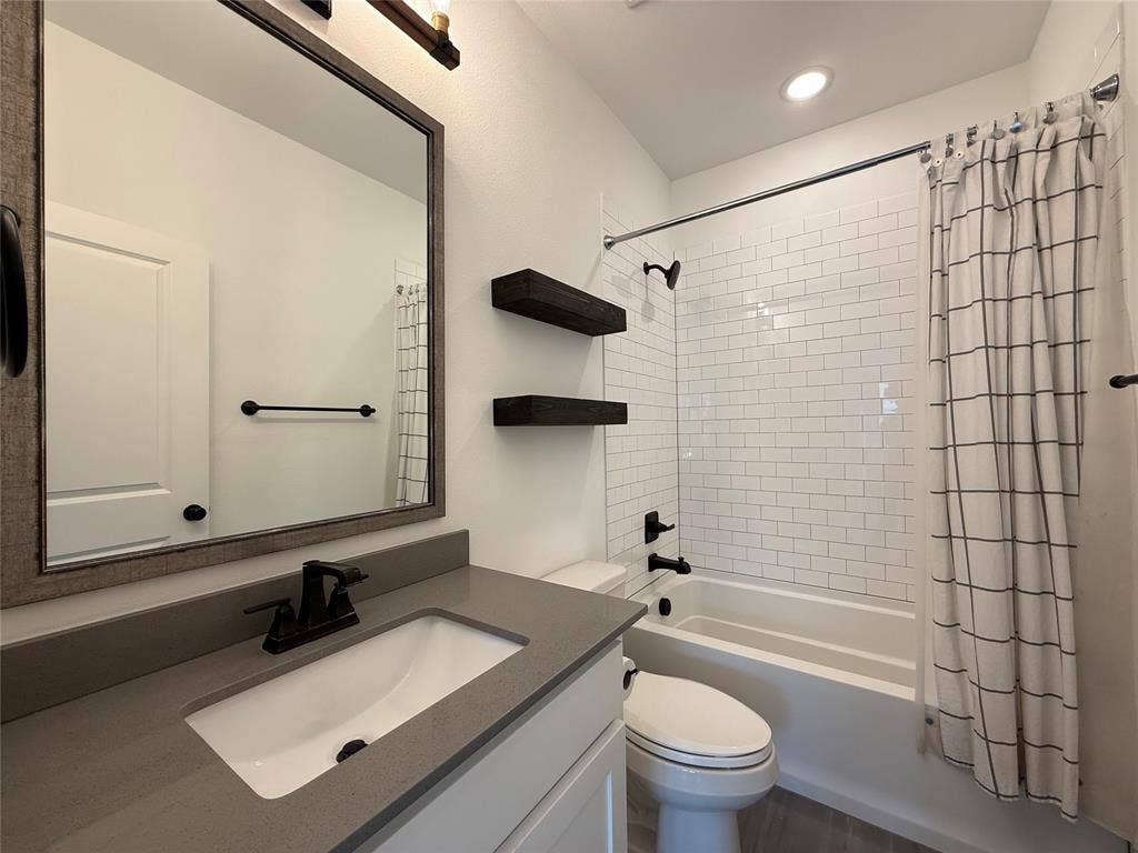12905 Yale Court, Frisco, TX 75035 Bathroom featuring a vanity with a solid-surface countertop, rectangular undermount sink, matte black hardware, white subway tile shower surround, and built-in floating shelves