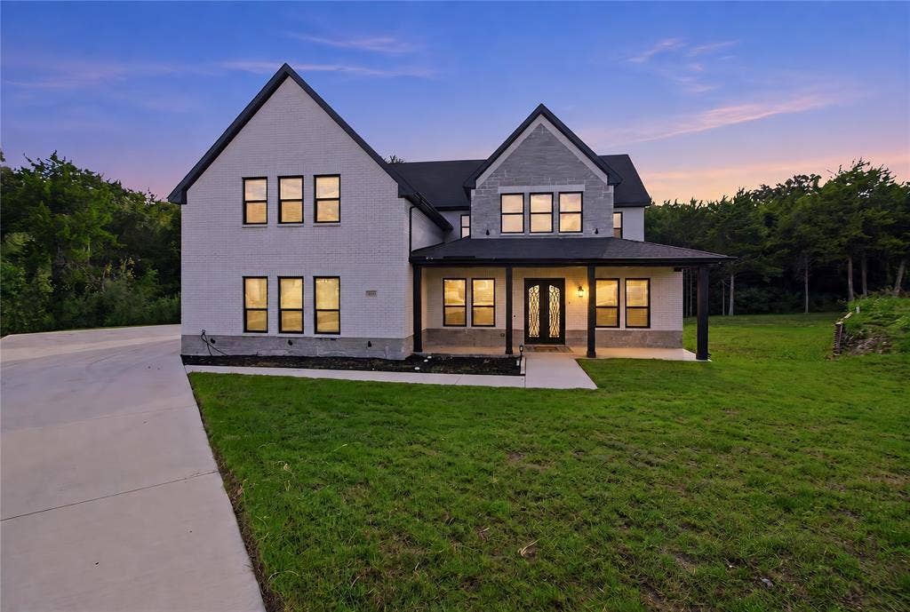 Multi-gabled exterior featuring painted brick and stone masonry, black-framed windows, a covered front porch, and an expansive concrete driveway
