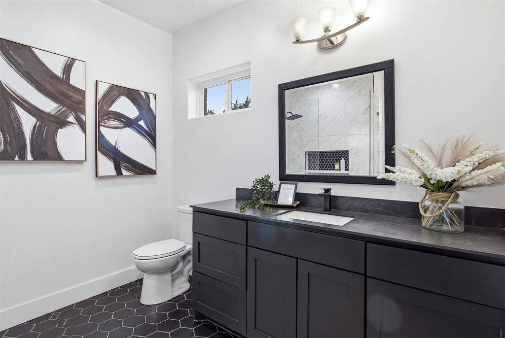 Bathroom featuring a matte black vanity with a rectangular undermount sink, dark stone-finish countertop, black-framed mirror, and black hexagonal tile flooring