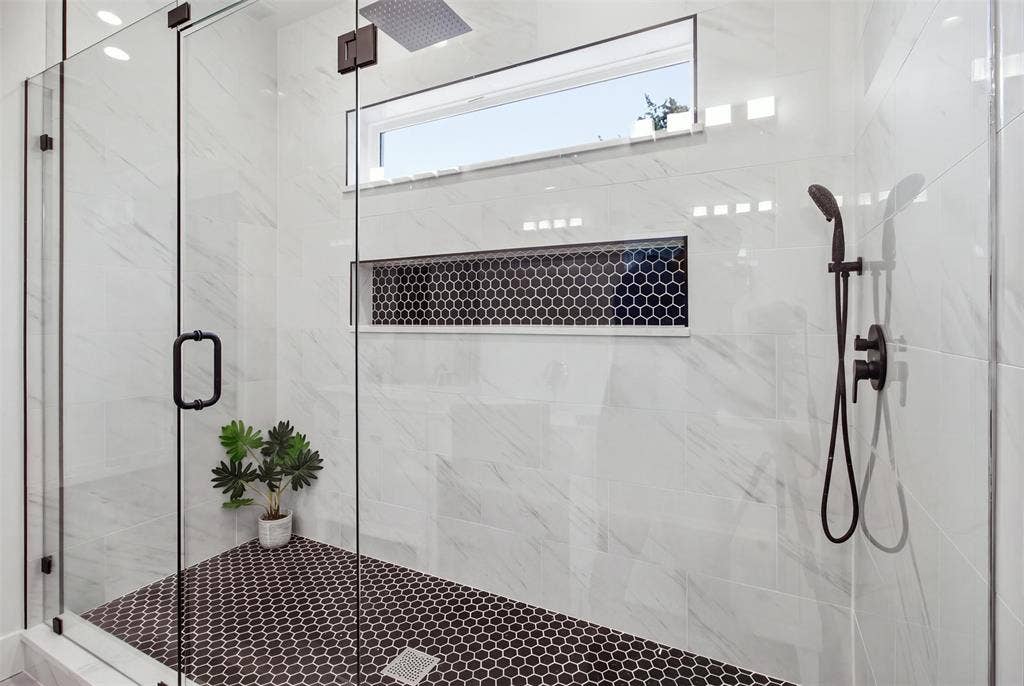 Walk-in shower featuring large-format wall tile, dark hexagonal floor tile, a recessed storage niche with decorative tile inlay, a ceiling-mounted rainfall showerhead, and a matte black handheld shower fixture