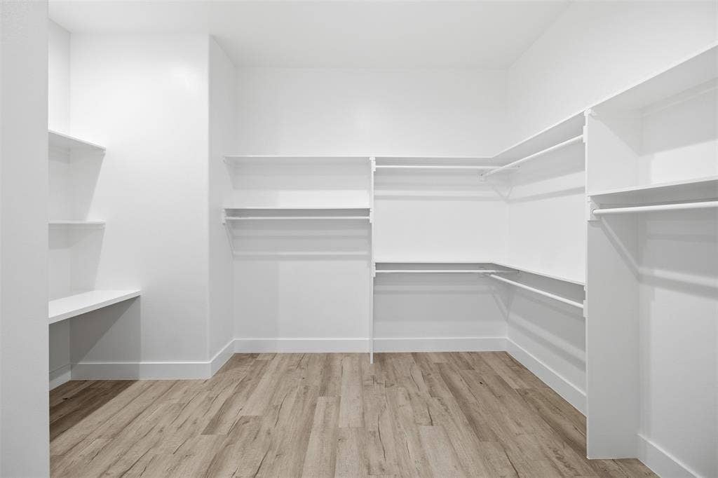 Walk-in closet featuring wood-finish flooring, white walls, and multi-level built-in shelving with integrated hanging rods