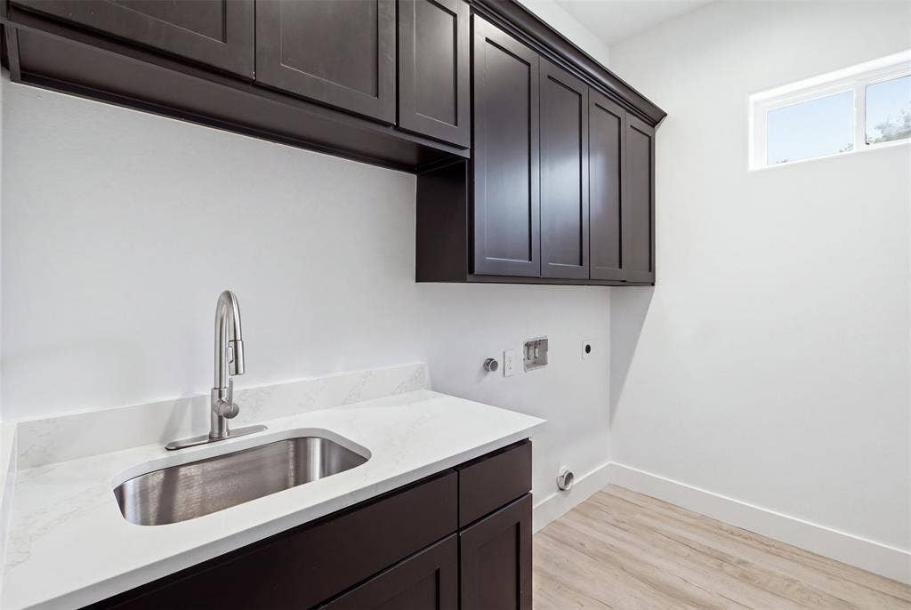 Dark cabinetry featuring built-in upper and lower storage, white stone-finish countertop, stainless steel undermount sink with a high-arch pull-down faucet, and light-toned wood-finish flooring