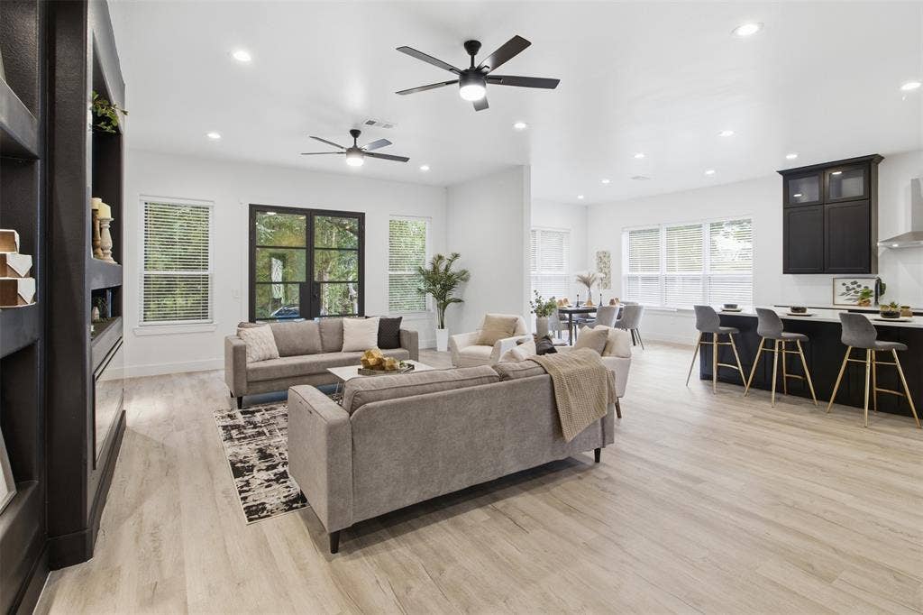 Open-concept interior featuring light wood-finish flooring, recessed lighting, dual ceiling fans, a dark built-in shelving unit, and a kitchen island with dark cabinetry