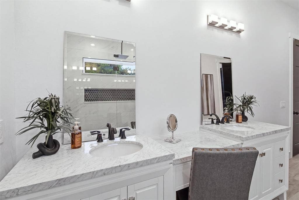 Dual-vanity bathroom featuring white cabinetry, stone-finish countertops, undermount sinks, wall-mounted light fixtures, and rectangular mirrors