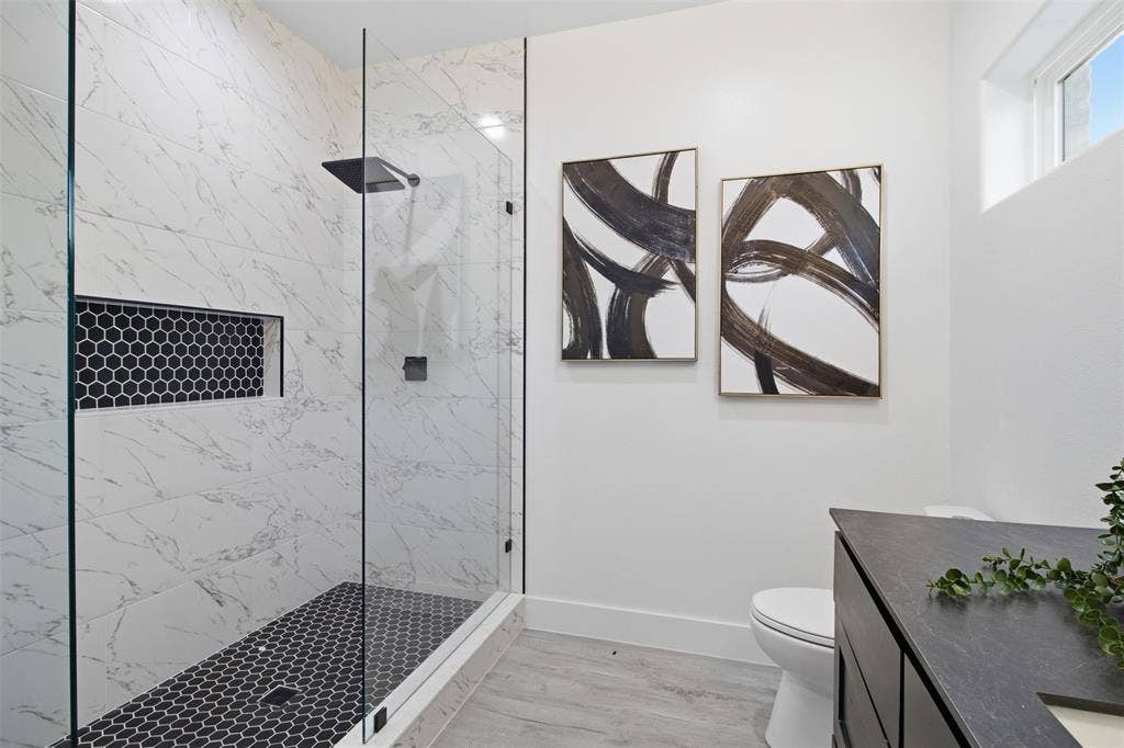 Walk-in shower featuring large-format stone-look wall tiles, a built-in hexagonal tile niche, and a glass partition