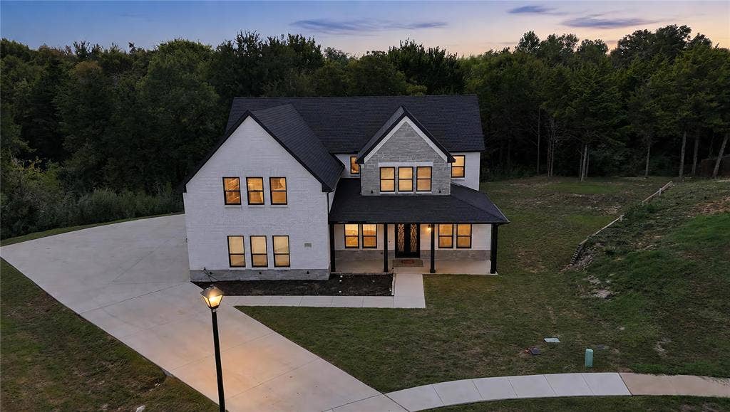 Two-story residence featuring a painted brick and stone exterior, steep-pitched shingle roof, covered front porch, and expansive concrete driveway
