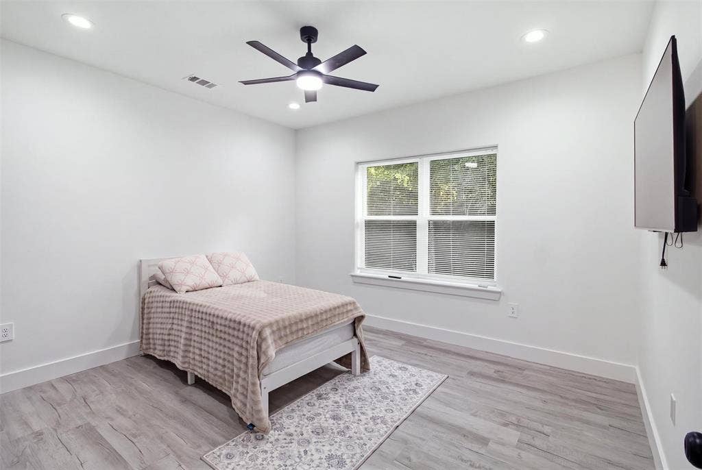 Wood-finish flooring, recessed lighting, matte black ceiling fan with integrated light, and large dual-pane window