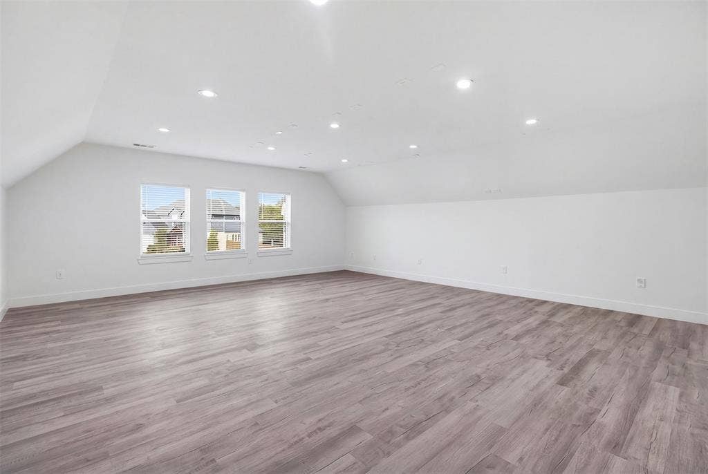Expansive media room featuring wood-finish flooring, vaulted ceilings, and recessed lighting