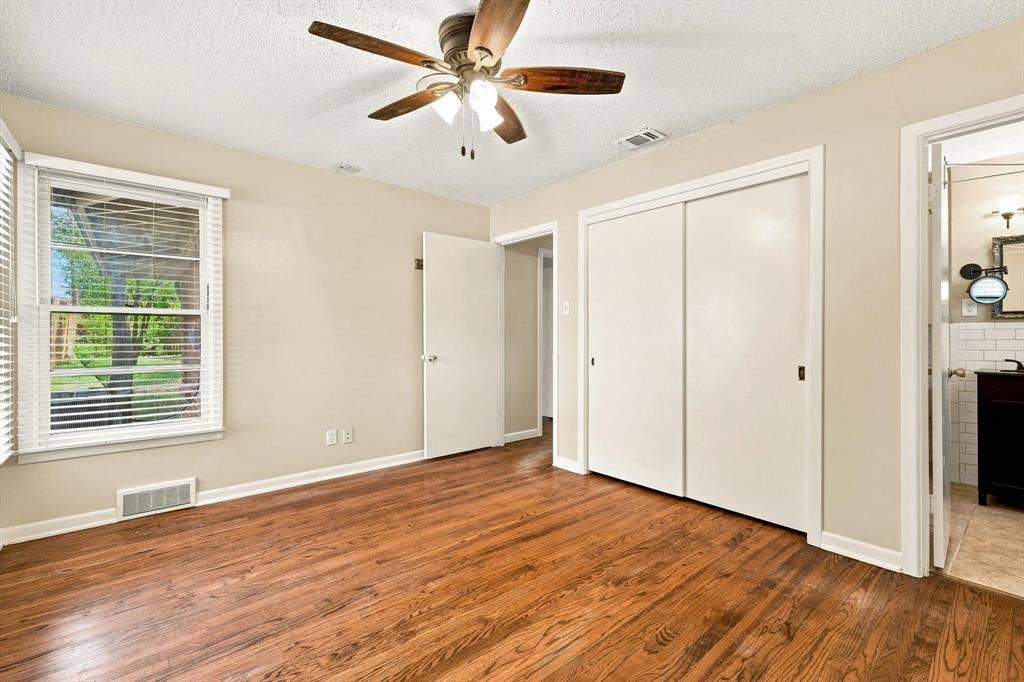 Room featuring wood-finish flooring, a multi-blade ceiling fan with integrated lighting, dual-panel sliding closet doors, and a window with horizontal blinds