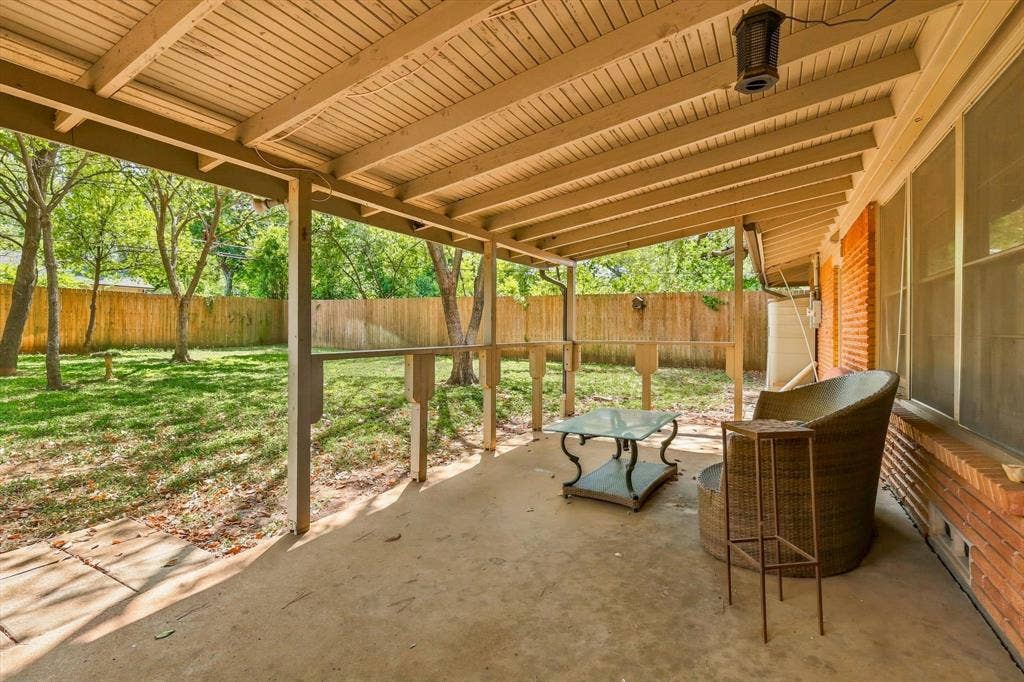 Covered patio featuring a concrete floor, beadboard ceiling, wooden support posts, and brick exterior walls, opening to a fenced backyard