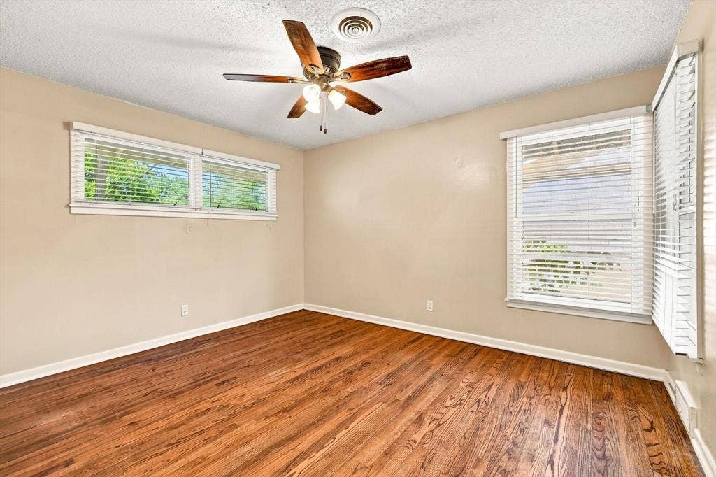 Room featuring wood-finish flooring, multiple windows with horizontal blinds, and a multi-blade ceiling fan with integrated lighting