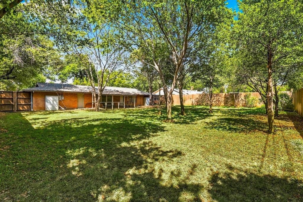 Expansive backyard featuring mature trees, a grass lawn, perimeter wood fencing, and an attached covered patio