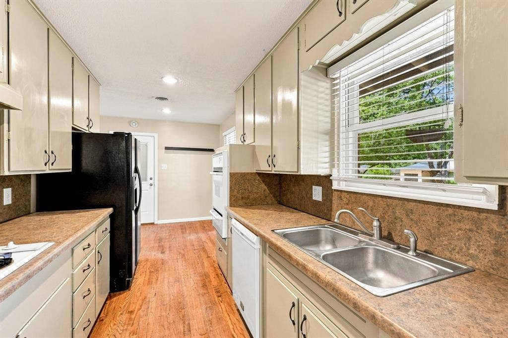 Kitchen featuring cabinetry with dark hardware, laminate countertops, wood-finish flooring, a double-basin stainless steel sink with a goose-neck faucet, and built-in wall oven