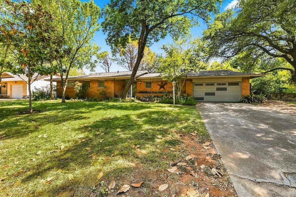 Single-story brick exterior featuring a multi-car garage, concrete driveway, and mature landscaping