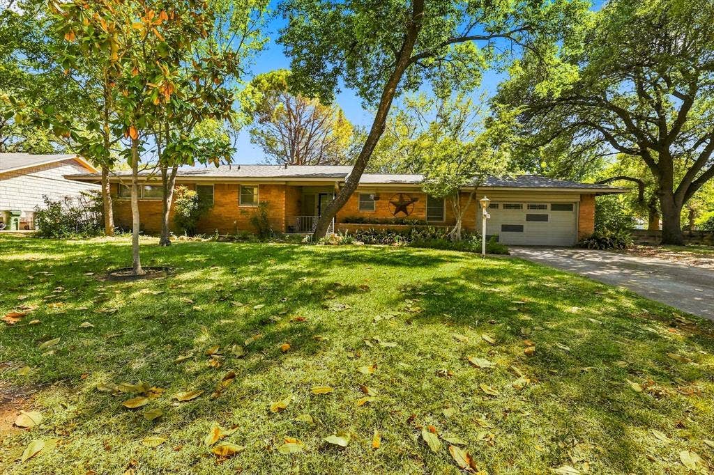 Single-story brick exterior featuring a multi-car garage, expansive lawn, and mature trees