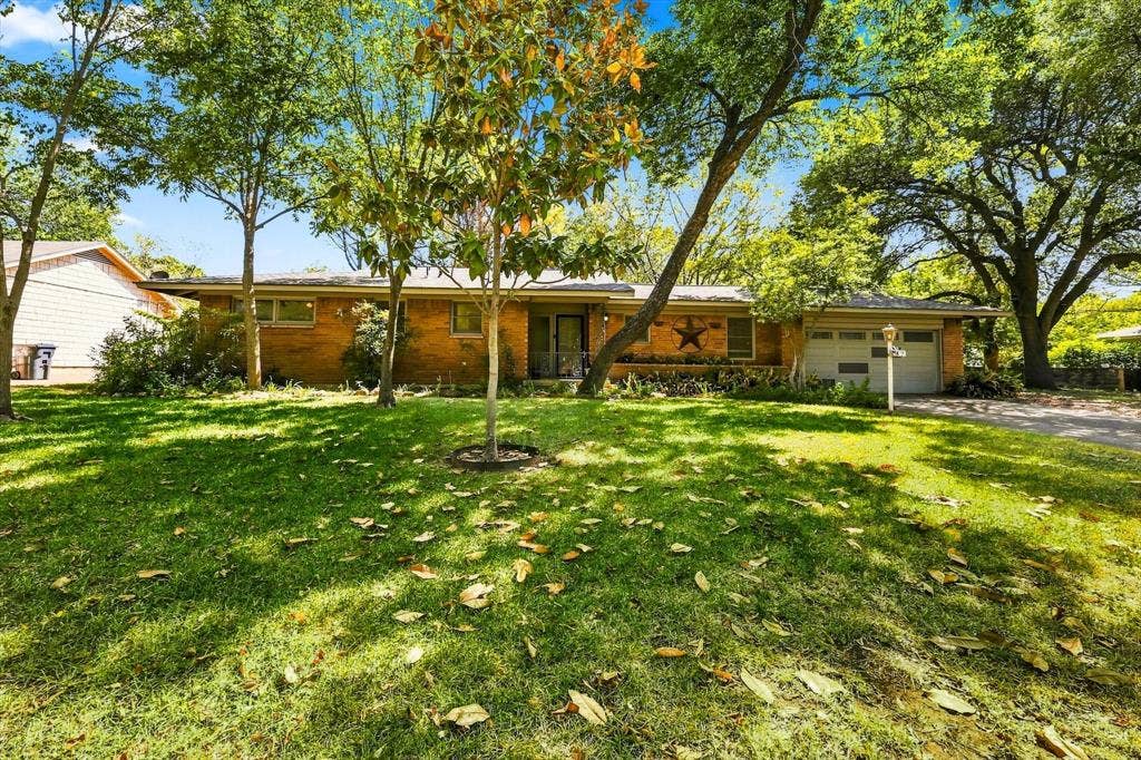 Single-story brick exterior featuring an attached two-car garage, mature landscaping, and an expansive lawn