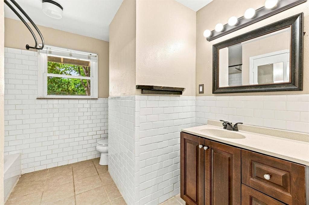 Bathroom featuring white subway tile wainscoting, dark-finish wood cabinetry, integrated countertop with oval sink, and a framed vanity mirror with integrated light fixture