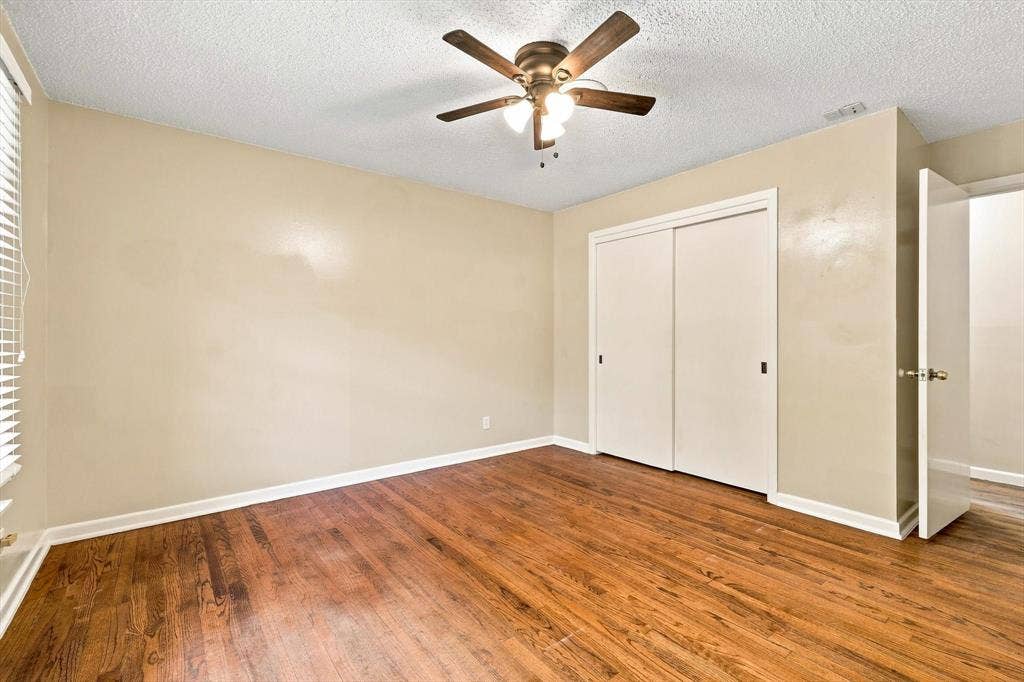Room featuring wood-finish flooring, a ceiling fan with integrated lighting, and a sliding-door closet