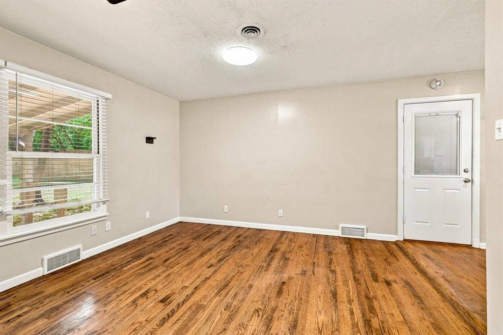 Wood-finish flooring, multi-pane window with horizontal blinds, and a white exterior door featuring a glass inset