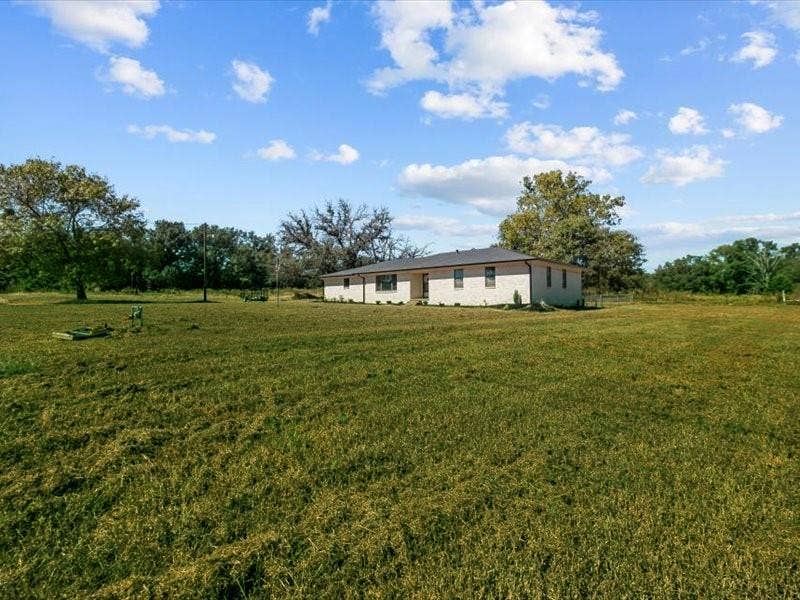 17014 Woodcrest Circle, Lindale, TX 75771 Single-story light-colored brick exterior featuring a low-pitched roof and expansive surrounding acreage with mature trees