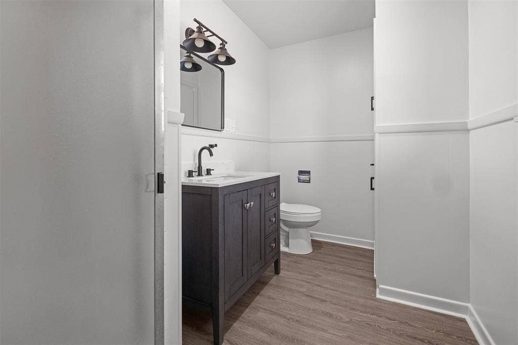 17014 Woodcrest Circle, Lindale, TX 75771 Dark wood-finish vanity with a light-toned countertop, rectangular sink, matte black faucet, wall-mounted mirror, and wood-finish flooring