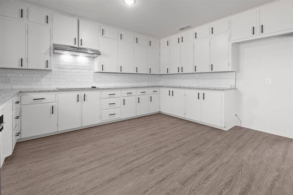 17014 Woodcrest Circle, Lindale, TX 75771 Kitchen featuring white shaker-style cabinetry with matte black hardware, stone-patterned countertops, a white brick-pattern backsplash, stainless steel range hood, and wood-finish flooring