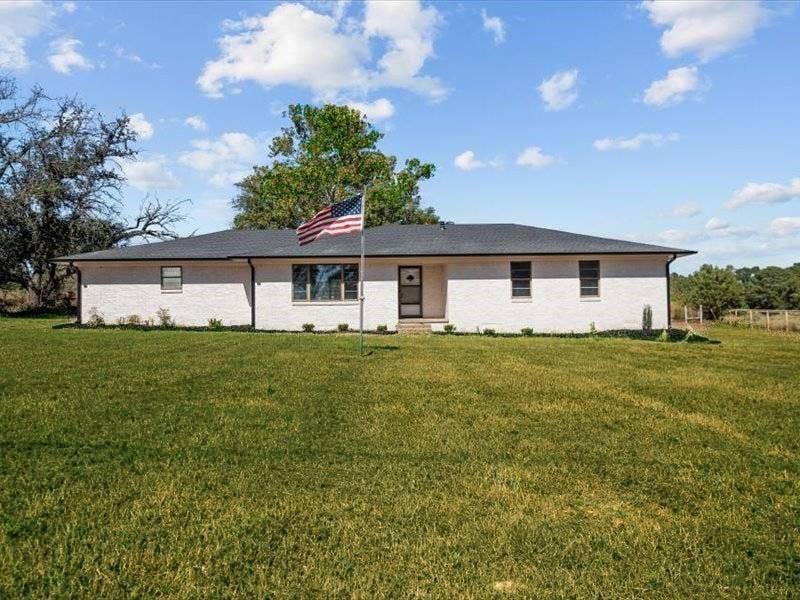 17014 Woodcrest Circle, Lindale, TX 75771 Single-story residence featuring a painted brick exterior, dark-toned hip roof, and expansive front lawn