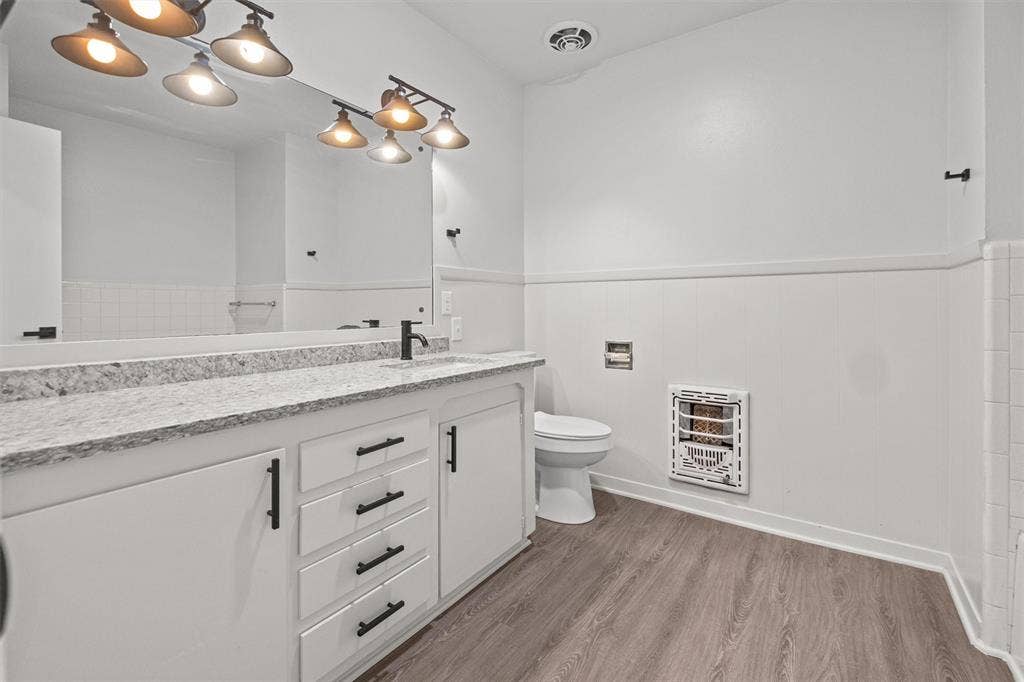 17014 Woodcrest Circle, Lindale, TX 75771 Bathroom featuring a stone-composite countertop, white vanity cabinetry with matte black hardware, integrated wall-mounted heater, wood-finish flooring, and multi-light vanity fixture