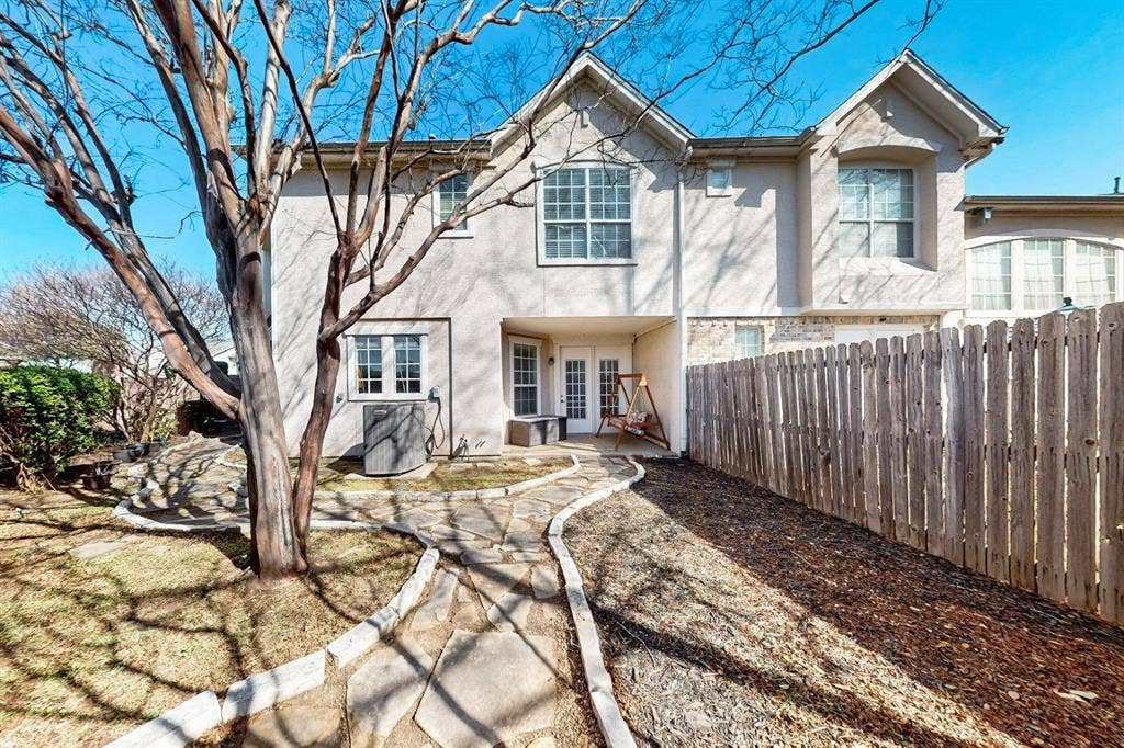 2606 Rue De Ville, Irving, TX 75038 Rear exterior featuring stucco siding, multi-gabled roofline, irregular stone pathway, and wood privacy fencing
