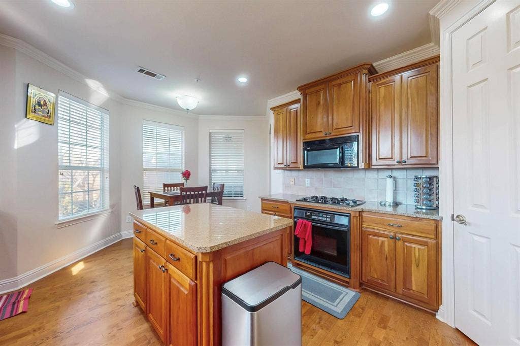 2606 Rue De Ville, Irving, TX 75038 Kitchen featuring wood cabinetry, stone countertops, central island, gas cooktop, and wood-finish flooring