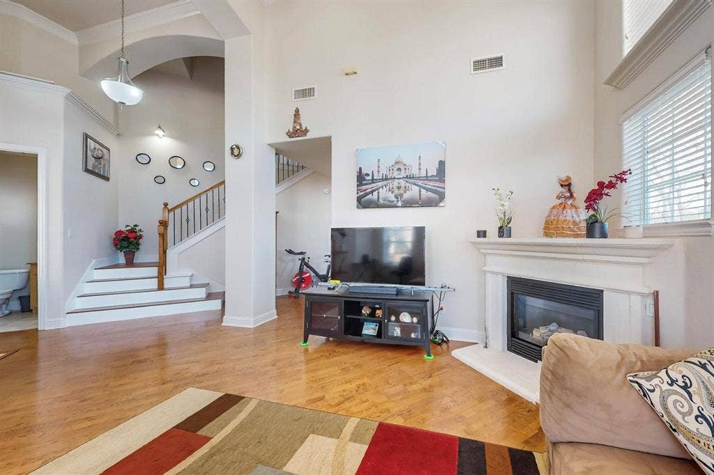 2606 Rue De Ville, Irving, TX 75038 High ceilings featuring architectural archways, wood-finish flooring, a fireplace with a decorative mantel, and a staircase with a wooden handrail and metal balusters