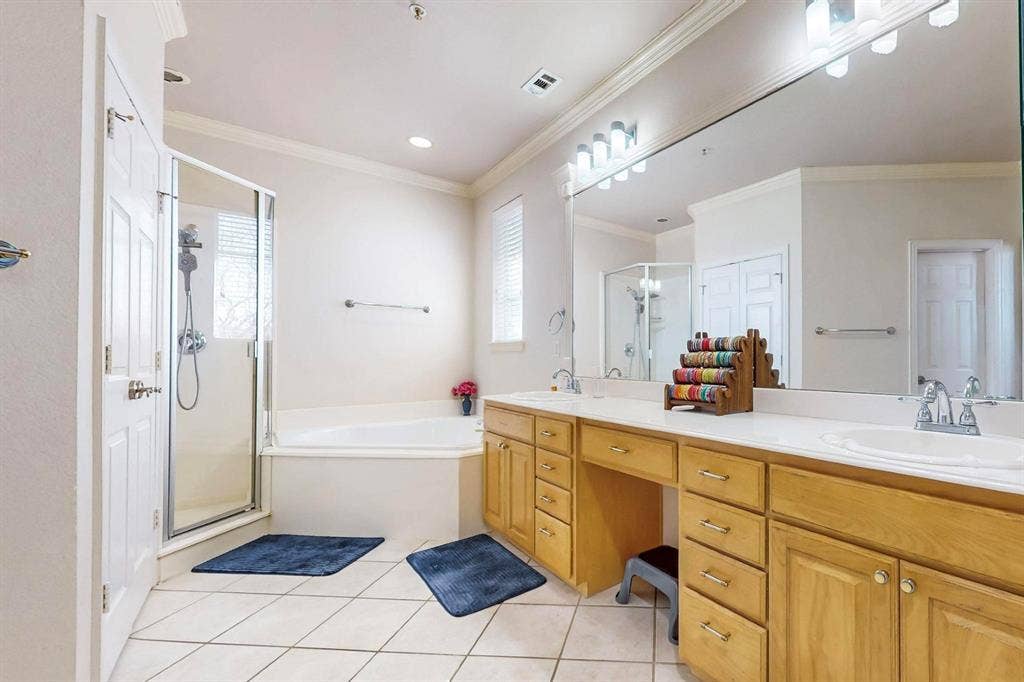 2606 Rue De Ville, Irving, TX 75038 Bathroom featuring a soaking tub, a separate glass-enclosed shower, light wood cabinetry, a dual-sink vanity with a solid-surface countertop, and ceramic tile flooring
