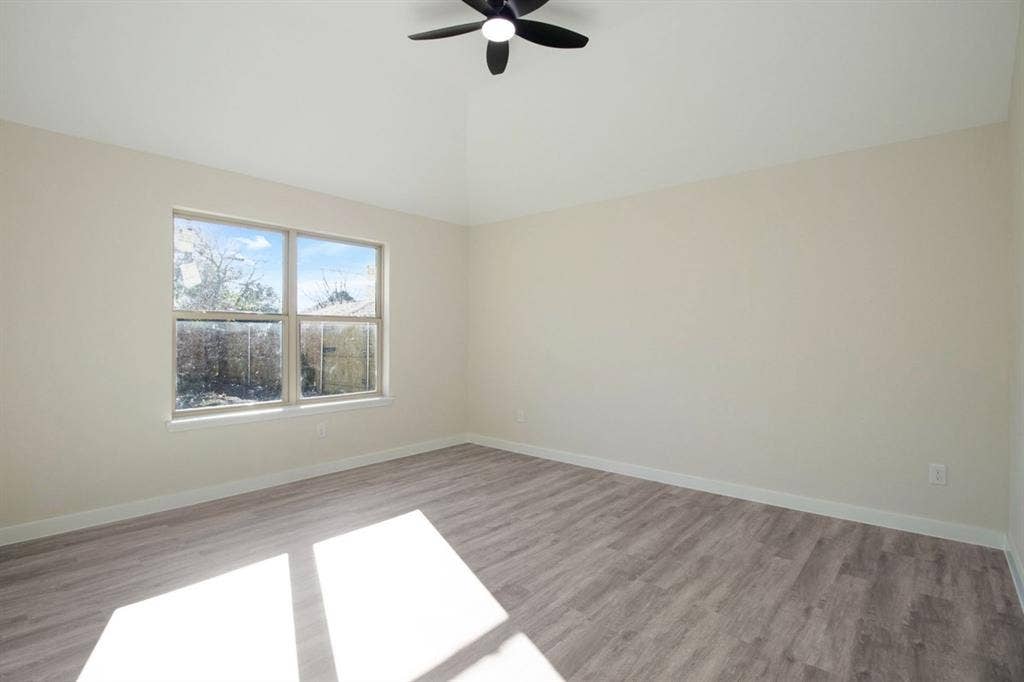 Vaulted ceiling with a ceiling fan, light-toned walls, and wood-finish flooring