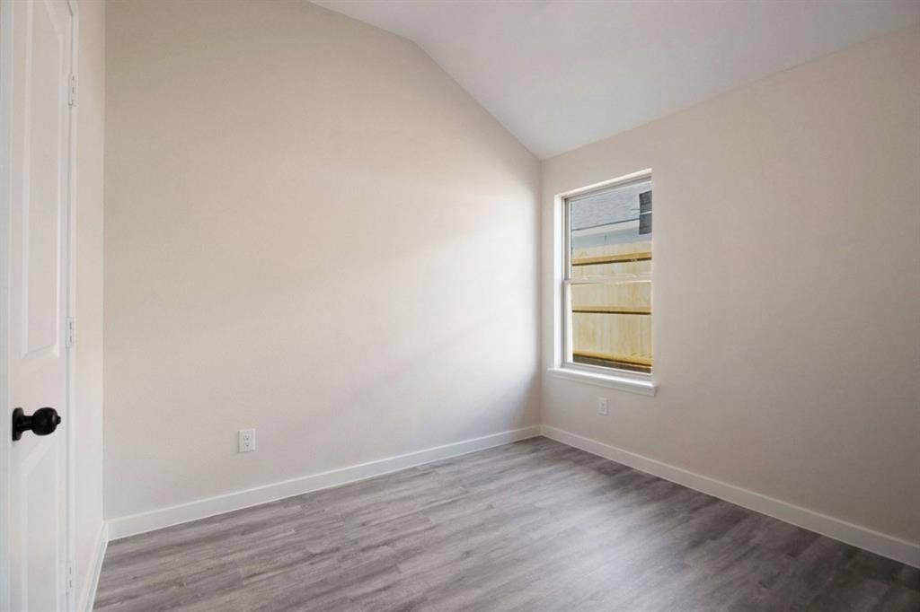 Vaulted ceiling with wood-finish flooring, a single window, and a white door with black hardware