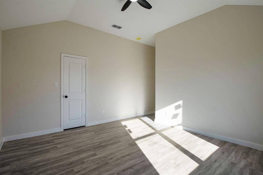 Bright, light-filled bedroom with wood-finish flooring, vaulted ceiling with ceiling fan, and white six-panel closet door