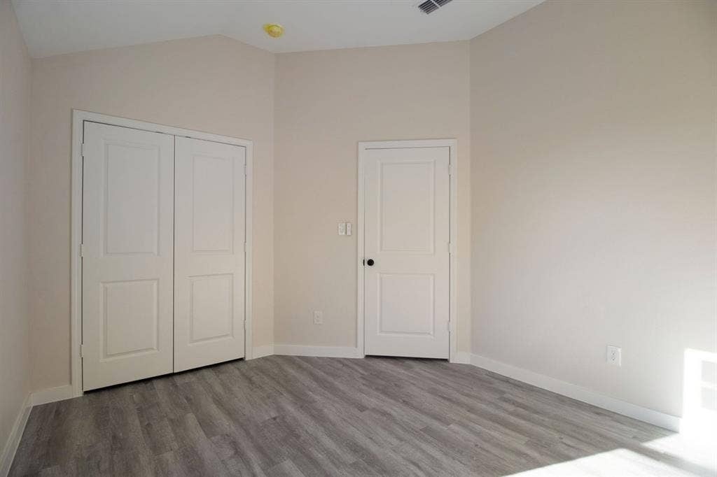 Vaulted ceiling, two-panel interior doors, light gray wood-finish flooring, and crisp white baseboards