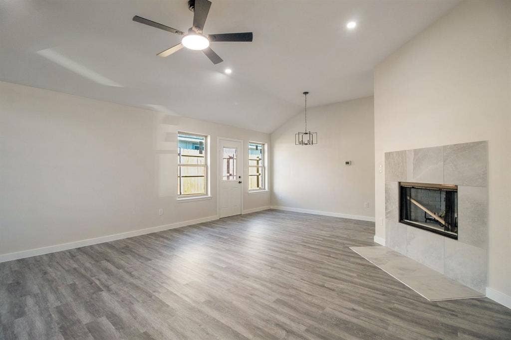 Vaulted ceiling, wood-finish flooring, white walls, built-in fireplace with tile surround, and an exterior door with integrated windows