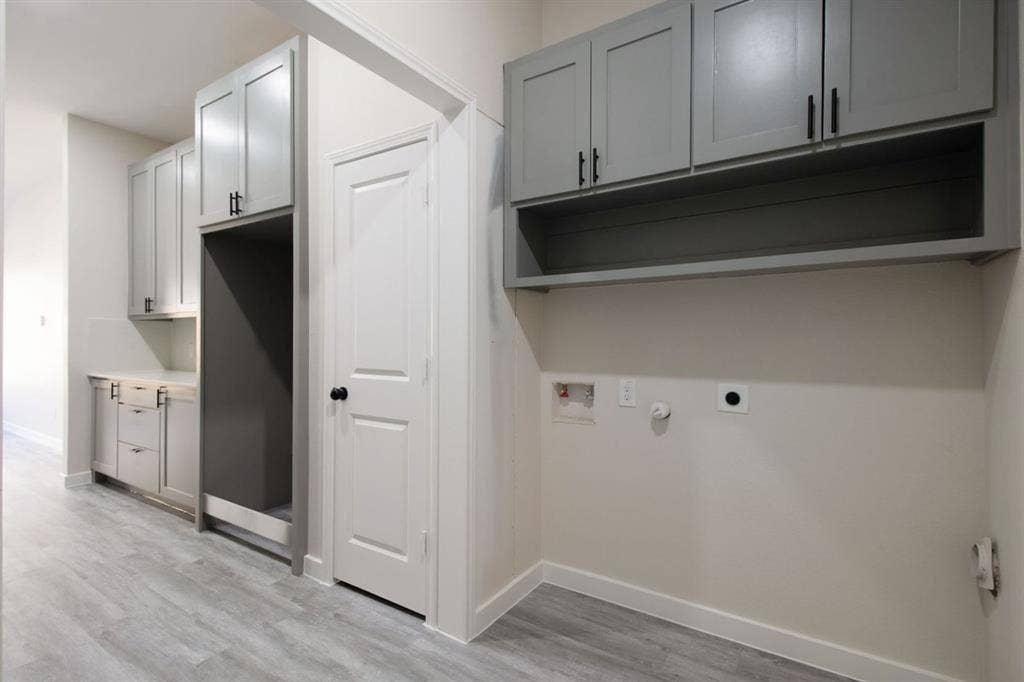 Wood-finish flooring, built-in cabinetry with matte black hardware, integrated appliance space, and dedicated laundry hookups