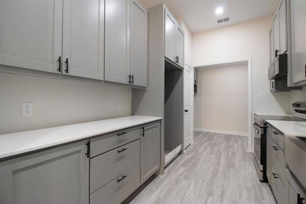 Galley kitchen featuring shaker-style cabinetry with matte black hardware, light-toned countertops, and wood-finish flooring